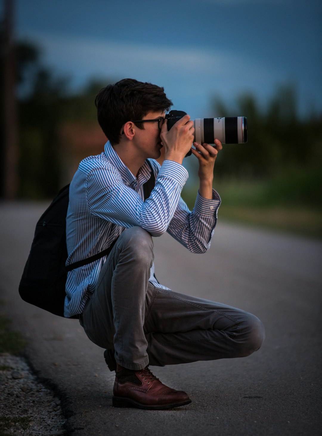 man-in-blue-and-white-striped-dress-shirt-and-gray-pants-sitting-on-gray-concrete-pavement-muettx0vkuq